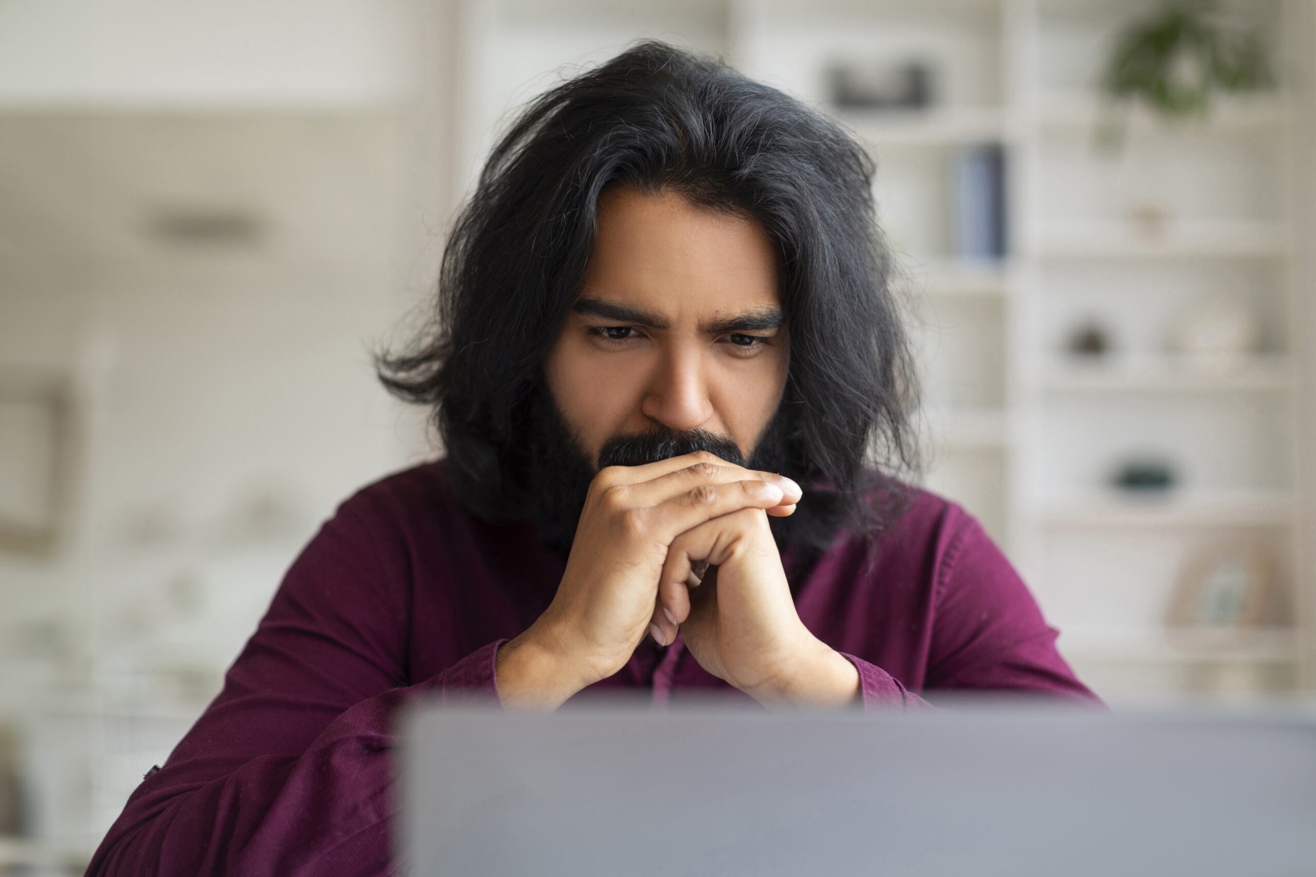 Brainstorming Concept. Thoughtful Indian Man Sitting At Workplace And Looking At Laptop Screen, Pensive Eastern Male Freelancer Working With Computer At Desk, Thinking About Problem Solution